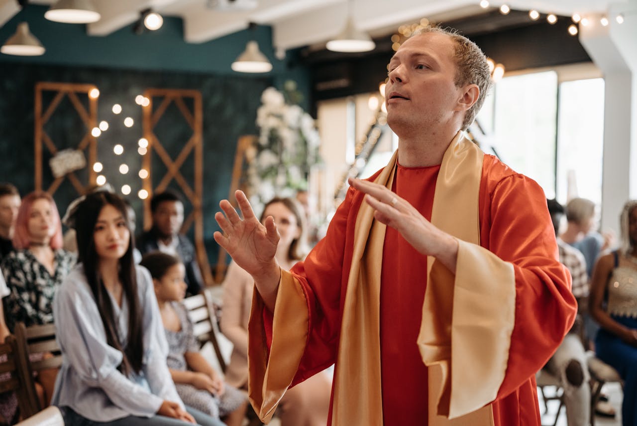 Man in red gown leading a spiritual gathering indoors with attentive congregation.